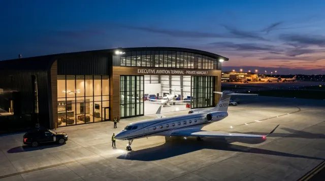 Vista exterior de un hangar de aviación ejecutiva de ultra-lujo al atardecer con un Gulfstream G700 en la plataforma, simbolizando la exclusividad global.