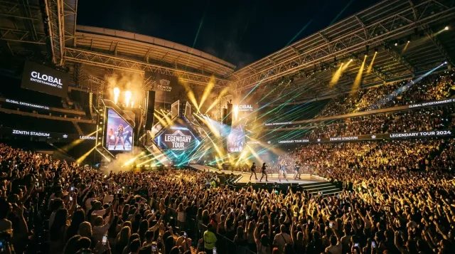 Estadio monumental abarrotado con una espectacular producción de luces y láseres, simbolizando las históricas y lucrativas giras mundiales de la reina del pop.
